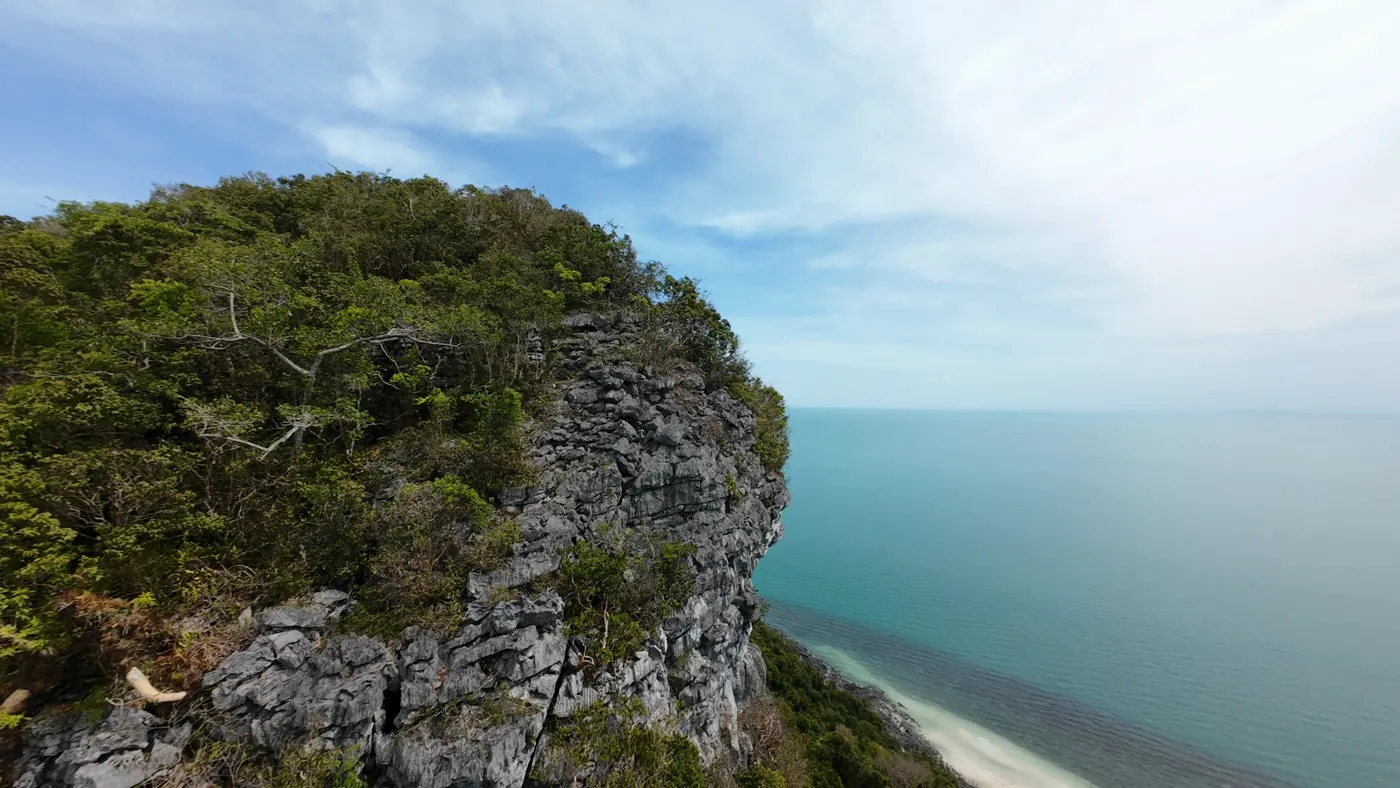 FPV drone passing a limestone cliff above a white-sand beach