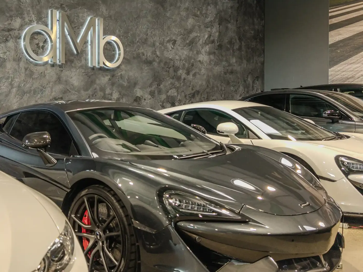 Grey McLaren in front of the illuminated DMB logo wall