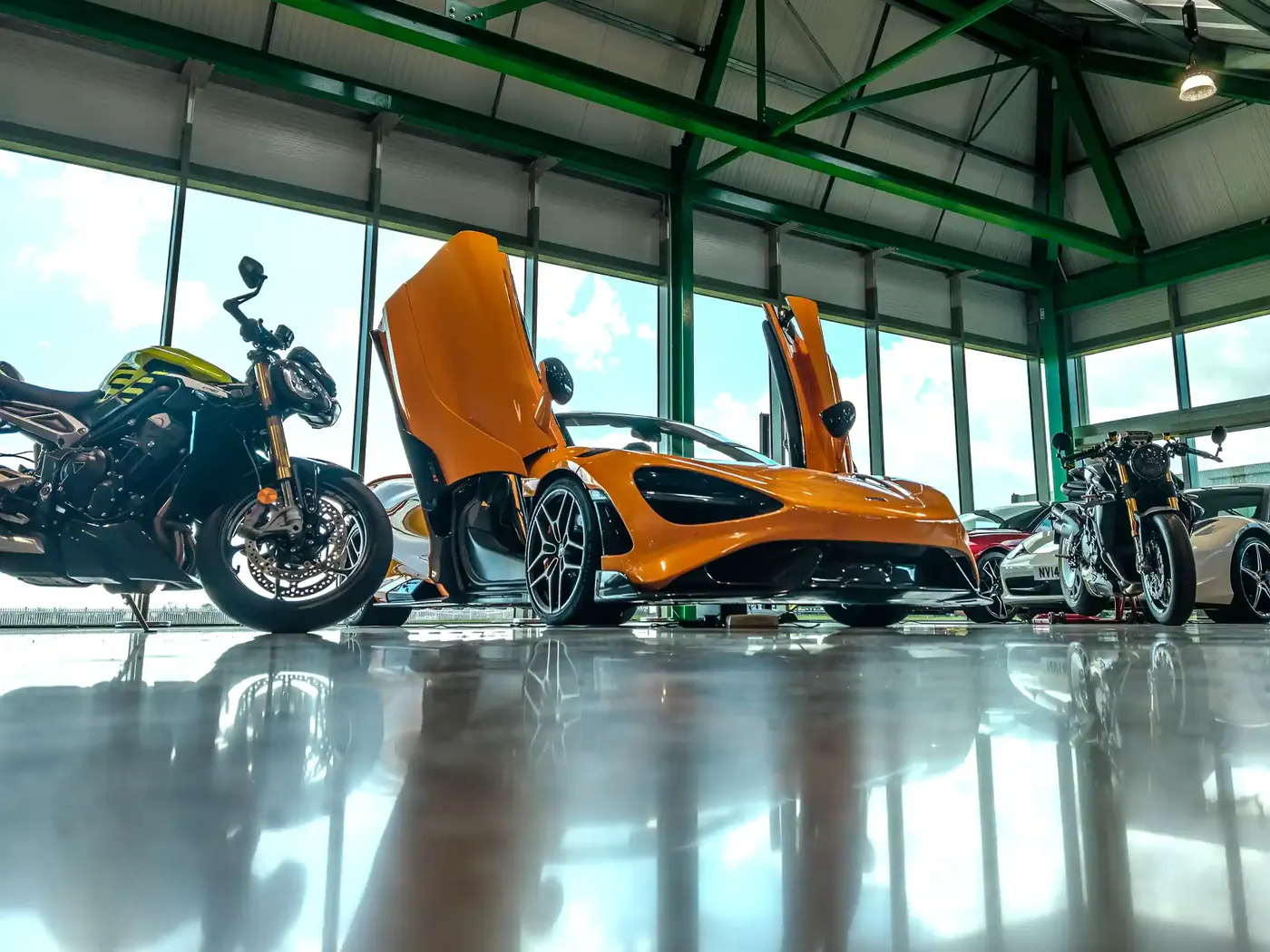 Orange McLaren with doors raised beside sports bikes in the DMB Collection showroom